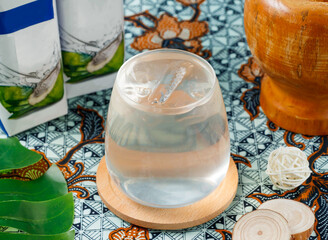 Refreshing coconut water served chilled on wooden coaster atop vibrant batik textile for natural hydration