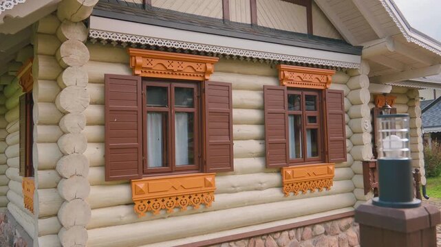 Beautiful facade of a traditional log cabin featuring ornate wooden carved window frames and brown shutters, showcasing rustic folk architecture and classic countryside building style