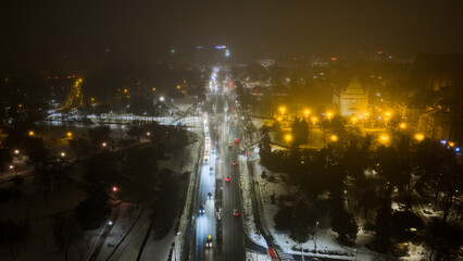 Widok z drona na nocne Stare Miasto w Toruniu, spowite delikatną mgłą. Podświetlone budynki i zabytkowa architektura lśnią w mgiełce, tworząc tajemniczy i nastrojowy miejski pejzaż.