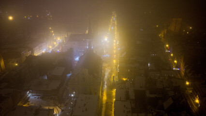 Widok z drona na nocne Stare Miasto w Toruniu, spowite delikatną mgłą. Podświetlone budynki i zabytkowa architektura lśnią w mgiełce, tworząc tajemniczy i nastrojowy miejski pejzaż. © Elżbieta Kaps