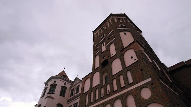 Impressive medieval mir castle architectural complex, a unesco world heritage site in belarus, viewed from a low angle with a dramatic gray cloudy sky providing a moody and historic atmosphere