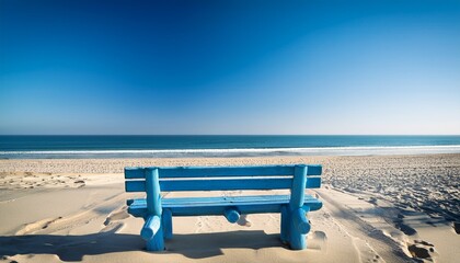 a blue wooden bench sits on a sandy beach with the ocean and clear sky in the background
