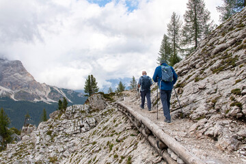 Fototapeta premium Hikers on path near Cinque Torri rock formation in Dolomite Alps or Pale Mountains named from carbonate rock dolomite in Veneto, Italy part of Limestone Alps near Cortina d'Ampezzo