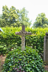 schön verziertes Steinkreuz inmitten von Efeu auf  dem Katholischen Friedhof in Kempten Allgäu