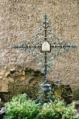 Wunderschön verziertes Eisenkreuz mit einem Heiligenbild vor einem großen Stein auf dem katholischen Friedhof in Kempten © Blende8