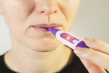 Woman measure temperature at home and hold electronic thermometer in mouth. High body temperature. Colds and flu concept.