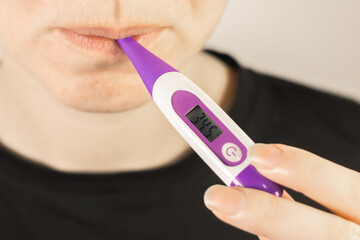 Woman is starting measure temperature at home with electronic thermometer in mouth.