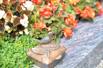 schönes Weihwassergefäß mit einem kleinen Vogel vor bunten Blumen auf dem Katholischen Friedhof in Kempten - Allgäu © Blende8