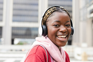 African American woman smiling on street red jacket pink hoodie backpack headphones copy space