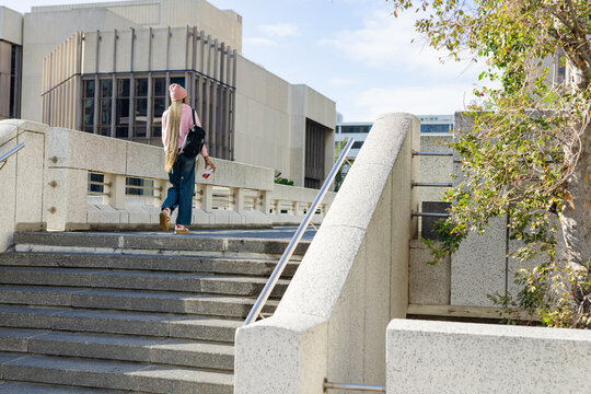 Person walking up concrete stairs carrying backpack and coffee cup on university campus