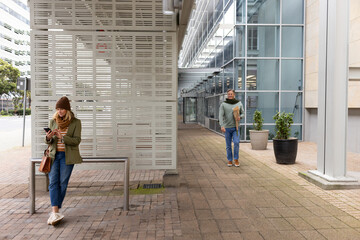 Senior couple waiting at bus shelter, checking smartphone and carrying grocery bag, copy space