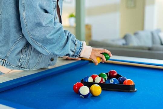 Person placing green billiard ball into rack on blue felt pool table in living room