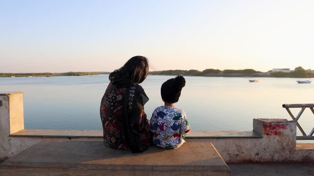 mother and child sitting on riverside bench enjoying peaceful sunset view