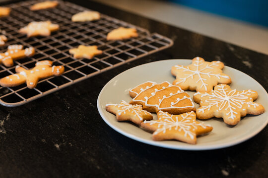 Light grey plate is holding iced gingerbread cookies on dark stone countertop with cooling rack