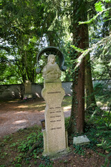 sehr alter schöner Grabstein mit Jesusfigur unter einem Dach auf einem Waldfriedhof in Memmingen © Blende8