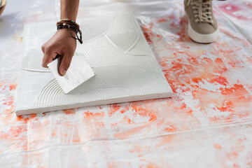 Indian male using notched trowel applying adhesive mortar onto tile on sheet during renovation