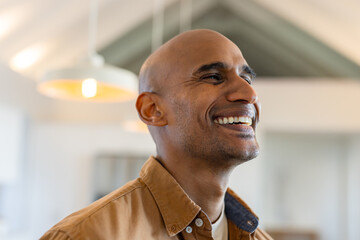 Adult African American man standing in loft room smiling near warm pendant lights and exposed beams