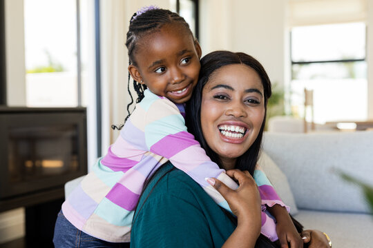 African American mother and daughter sharing warm hug while sitting in living room on sofa - Powered by Adobe
