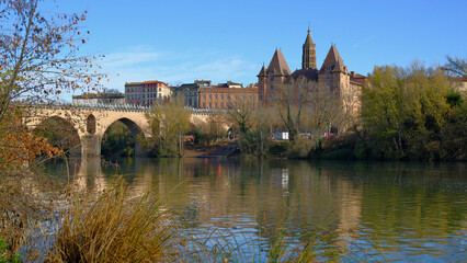 Obraz premium Charming Montauban with historical architecture and ancient stone bridge over tranquil river under clear blue sky during beautiful autumn day