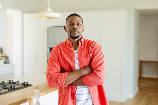 Mid-adult African American man leaning on island countertop in kitchen with cooktop, pendant lights - Powered by Adobe