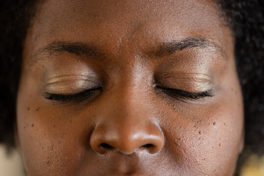 African American mid adult woman showcasing gold eyeshadow and mascara on closed eyelids in studio
