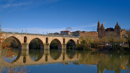 Obraz premium Montauban Stunning panoramic view of historic stone bridge spanning a tranquil river with charming architecture and clear blue sky, capturing the beauty of rural French landscape and heritage