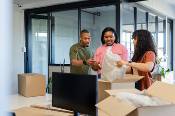 African American coworkers unpacking boxes and removing bubble wrap at office desk with monitor