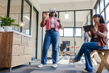 African American female coworkers testing VR headset while managing session with tablet at office