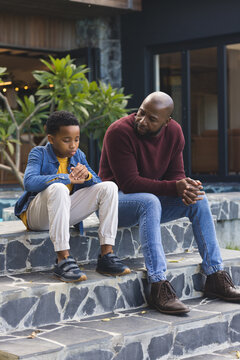 Mature African American father and son sitting on tile steps, son fidgeting by sliding door
