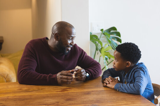 African American father and son in sweater and denim shirt engaging in conversation at wooden table