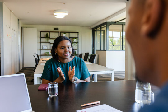 African colleagues discussing at meeting table, woman in green top gesturing, laptop, pink phone