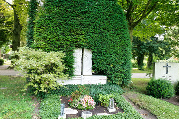 Der Grabstein steht inmitten einer sehr großen Hecke auf dem Waldfriedhof in Memmingen © Blende8
