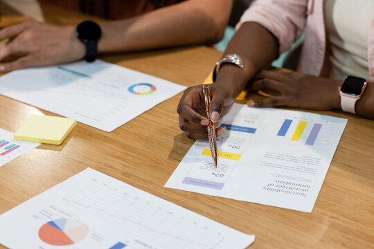 African American coworkers reviewing data on wood table woman wearing pink blazer holding metal pen