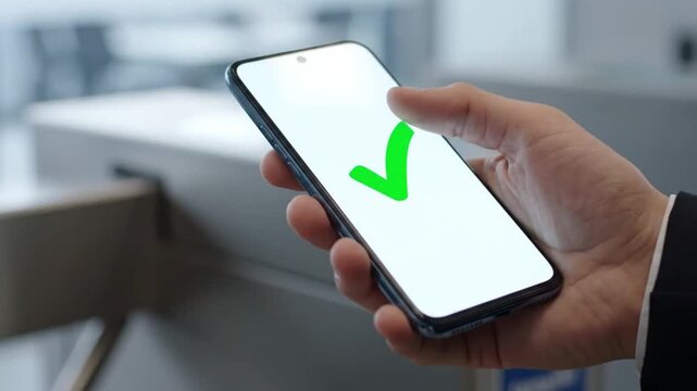 Close-up Hand holding smartphone with green checkmark on white screen, tapping to confirm. Mobile app success, digital validation, secure transaction.