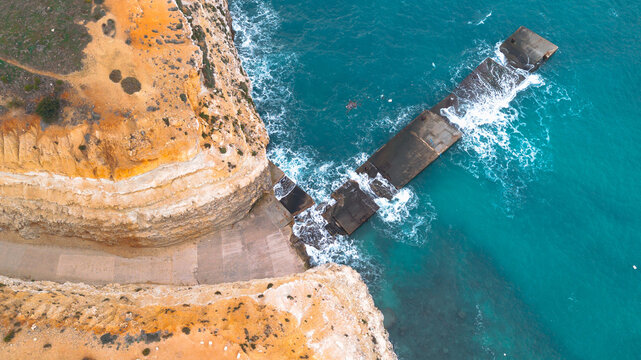 Aerial view of the rocky coastline and a pier in Malta, with azure water and a clear sky.
