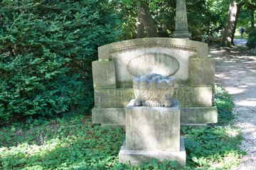 Grabstein in Form einer Bank und davor ein Stein mit einem steinernen Blumenkorb auf einem Friedhof in Ulm © Blende8