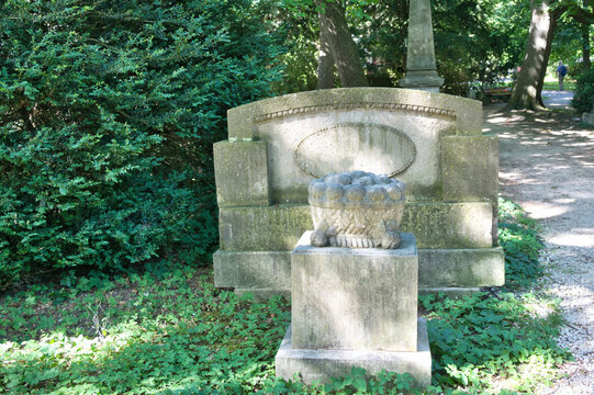 Grabstein in Form einer Bank und davor ein Stein mit einem steinernen Blumenkorb auf einem Friedhof in Ulm