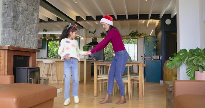 Mother and daughter entering home wearing festive headgear, spinning, clapping, celebrating holiday