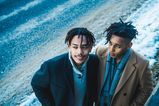 Stylish young men with dreadlocks looking up from snowy pavement. - Powered by Adobe