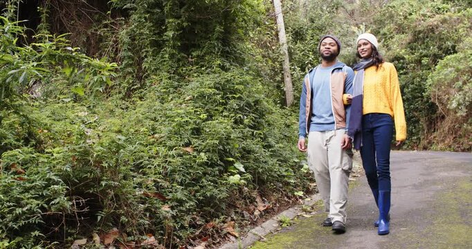 African American man and woman walking linked arms for leisure on paved forest trail, copy space