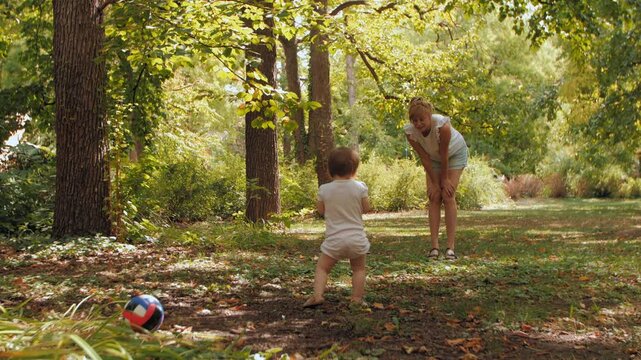 Little baby girl making first steps playing with mom in the park