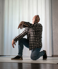 Young guy in a dancing pose on a white background. Modern dance in a plaid shirt. Sports plastic movements of arms and legs and body.