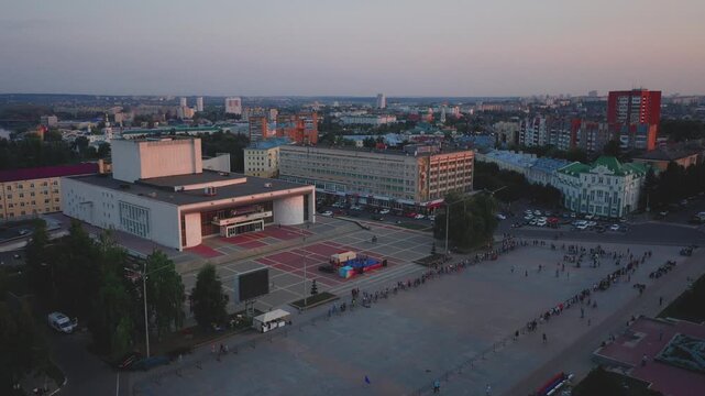 Aerial evening view of Orel city in Russia with river, Strelka, main buildings, churches and roads. Beautiful cityscape with lights reflecting on water at sunset, showing urban architecture, skyline.