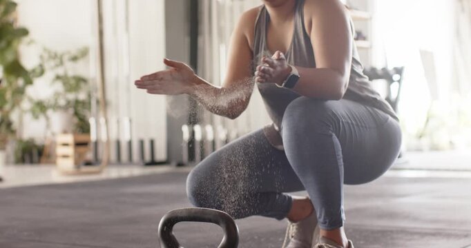 Woman is chalking palms, sending dust in gym, gripping 5kg kettlebell and lifting with hip hinge