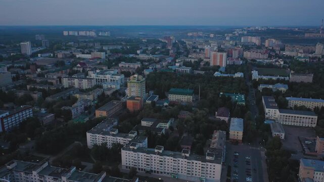 Aerial evening view of Orel city in Russia with river, Strelka, main buildings, churches and roads. Beautiful cityscape with lights reflecting on water at sunset, showing urban architecture, skyline.