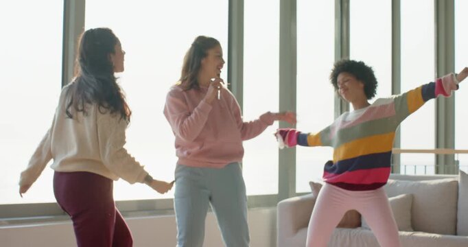 Picking up wireless microphones, Diverse female friends singing and dancing in living room for fun