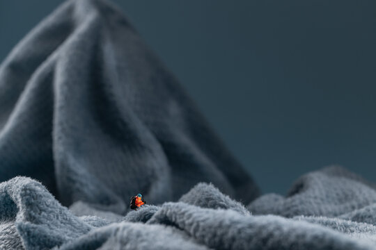 A miniature mountain climber figurine on a fuzzy fleece lining resembling a snow-covered surface, with a blurred background of a mountain or ice wall - Powered by Adobe