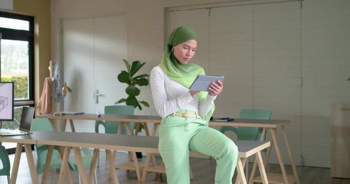 Entering office space, Indian woman sitting on trestle table, tapping tablet for content review