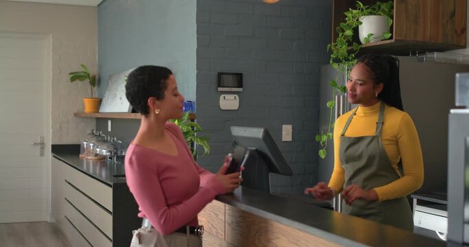Customer entering and scanning smartphone for payment on reader, cashier tapping till at counter