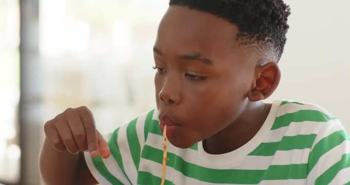 African American boy lifting spaghetti and slurping noodle while savoring sauce at home kitchen